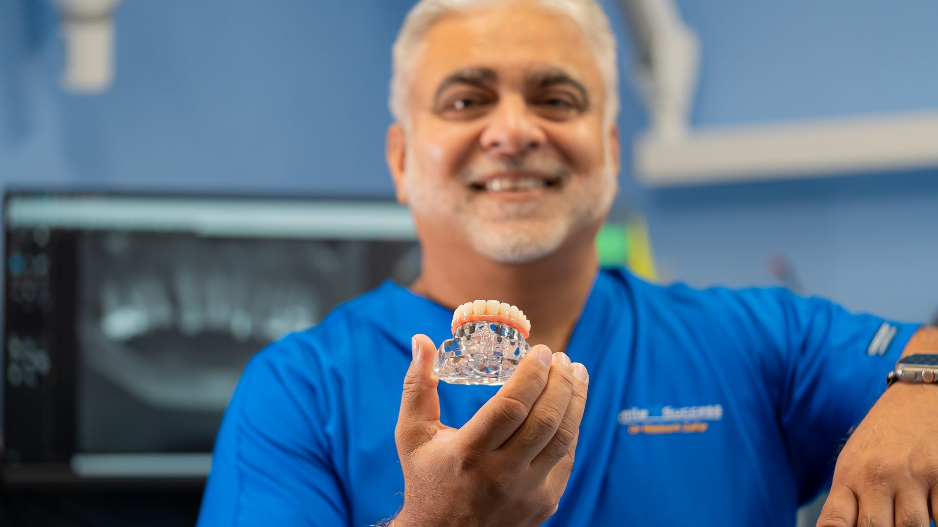 Dr Nadeem Zafar holding a full-arch zirconia implant bridge at Smile Success, Camberley